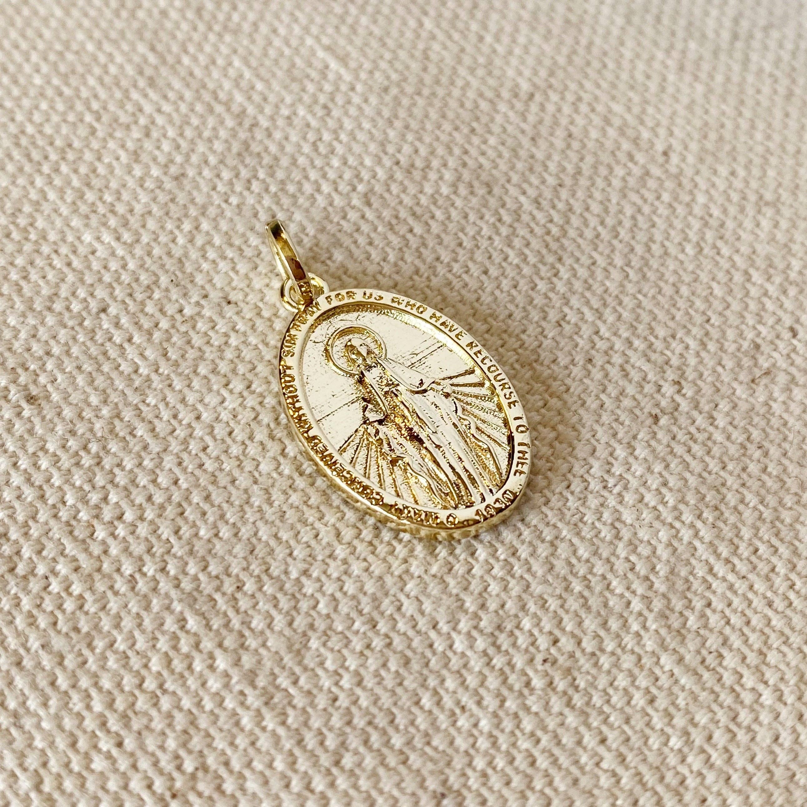 Gold pendant with religious design on a beige fabric background. 
Shop Rutledge Exchange for curated vintage and jewelry in Camden, SC.&nbsp;