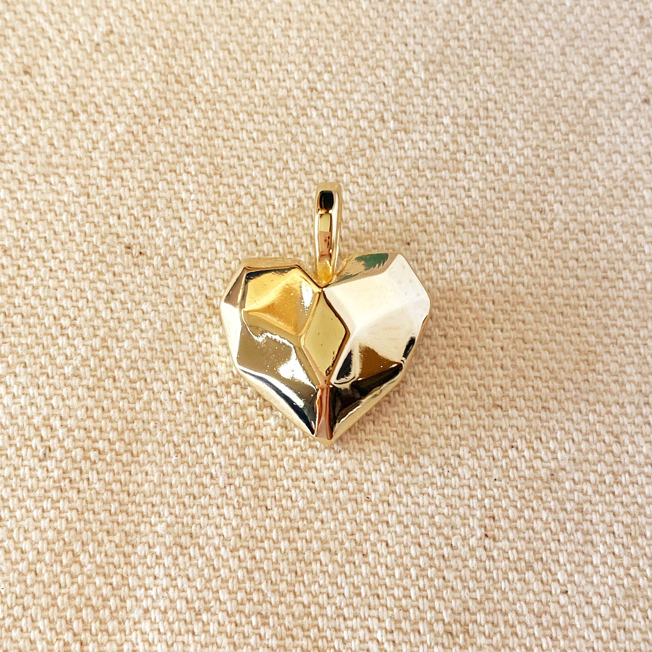 Gold geometric pendant on a beige fabric background. Shop Rutledge Exchange for curated vintage and jewelry in Camden, SC.