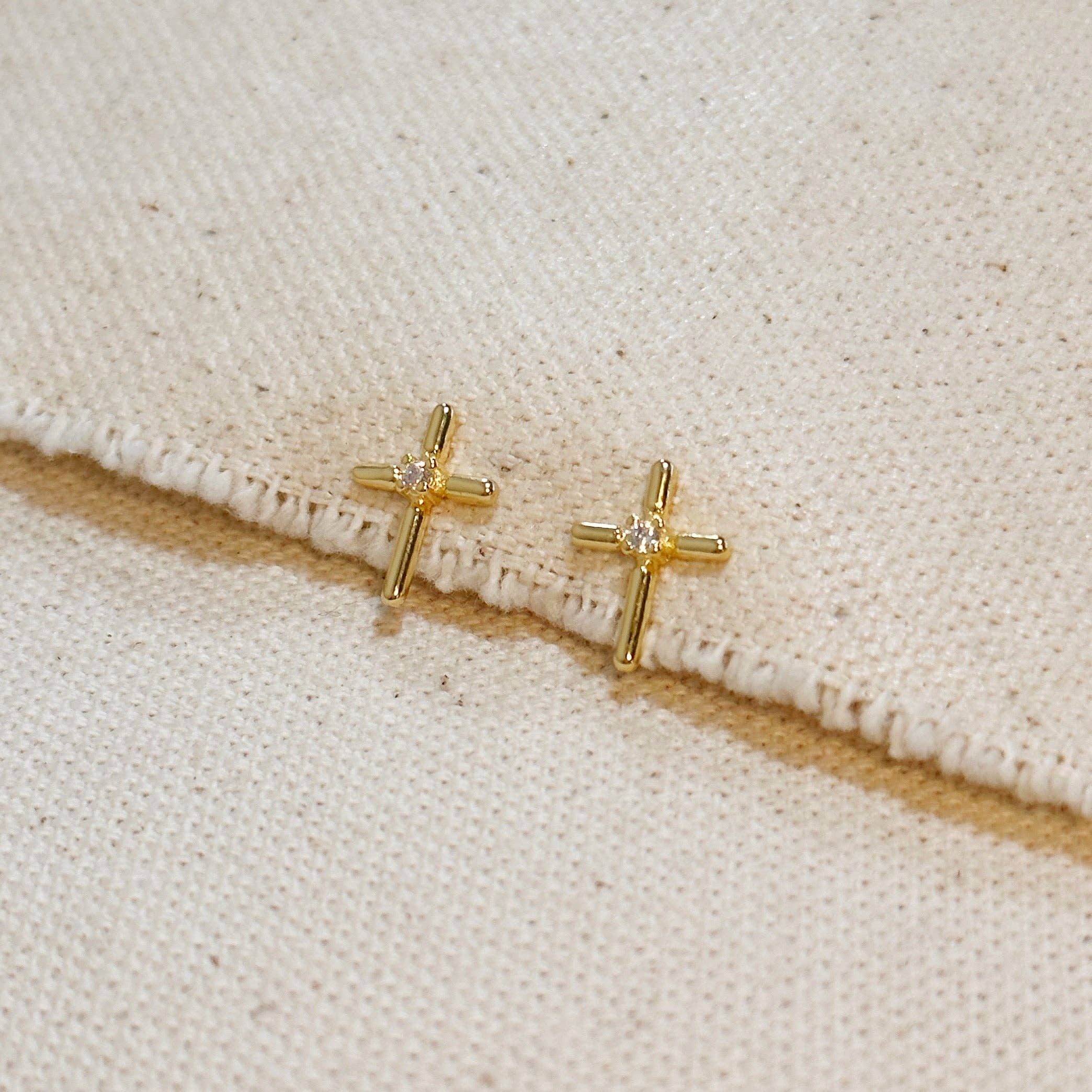 Gold cross earrings with clear stones on a beige fabric background