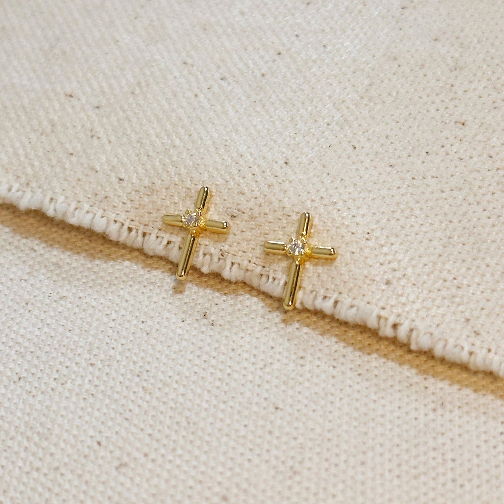 Gold cross earrings with clear stones on a beige fabric background
