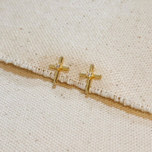 Gold cross earrings with clear stones on a beige fabric background