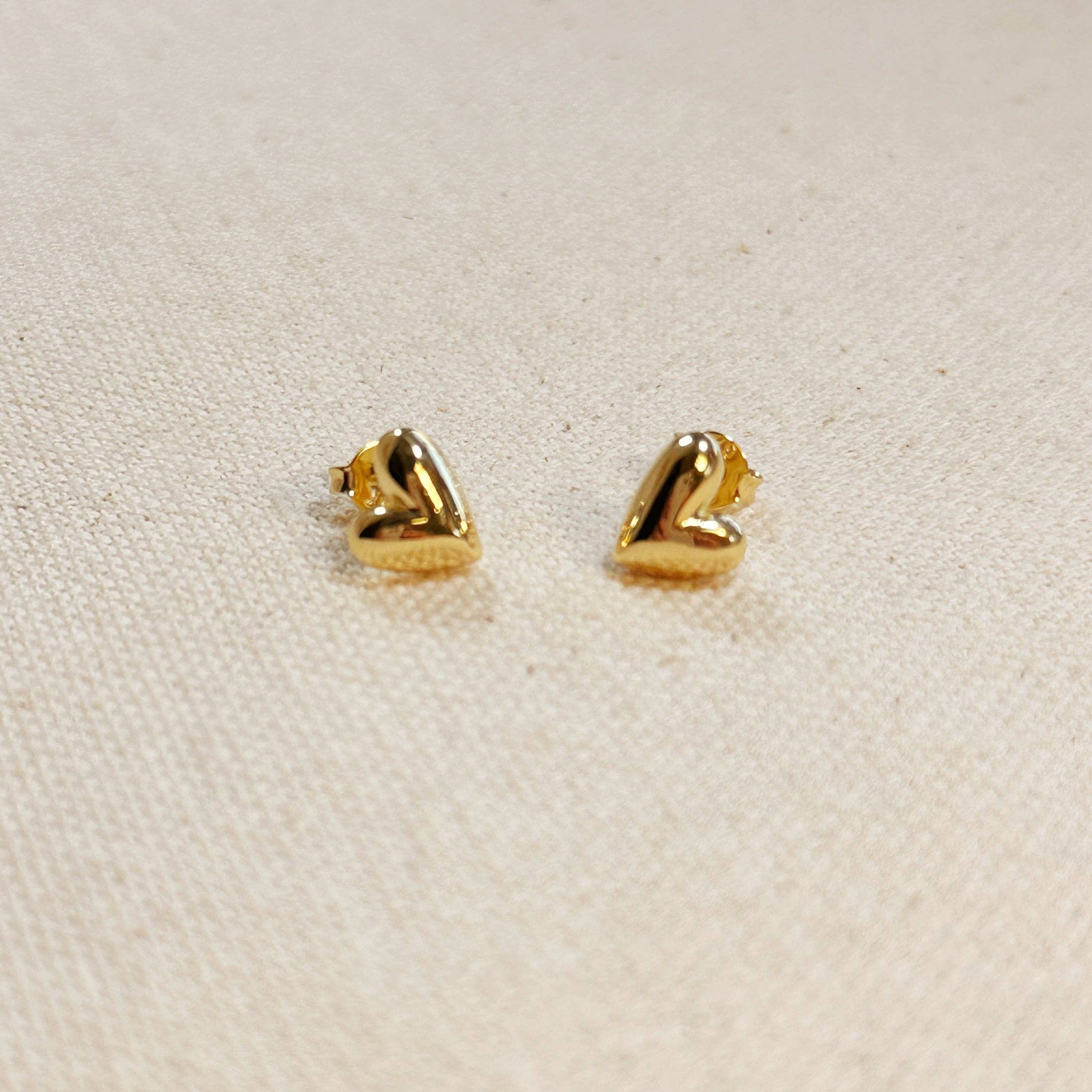 Pair of gold heart-shaped earrings on a beige fabric background. Shop Rutledge Exchange for curated vintage and jewelry in Camden, SC.