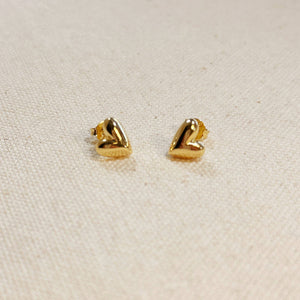 Pair of gold heart-shaped earrings on a beige fabric background. Shop Rutledge Exchange for curated vintage and jewelry in Camden, SC.