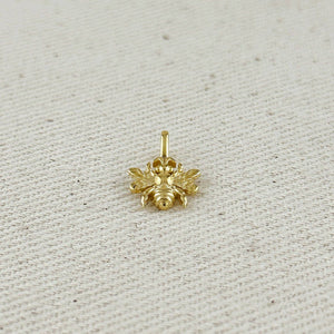 Gold bee-shaped pendant on a beige fabric background. Shop Rutledge Exchange for curated vintage and jewelry in Camden, SC.&nbsp;