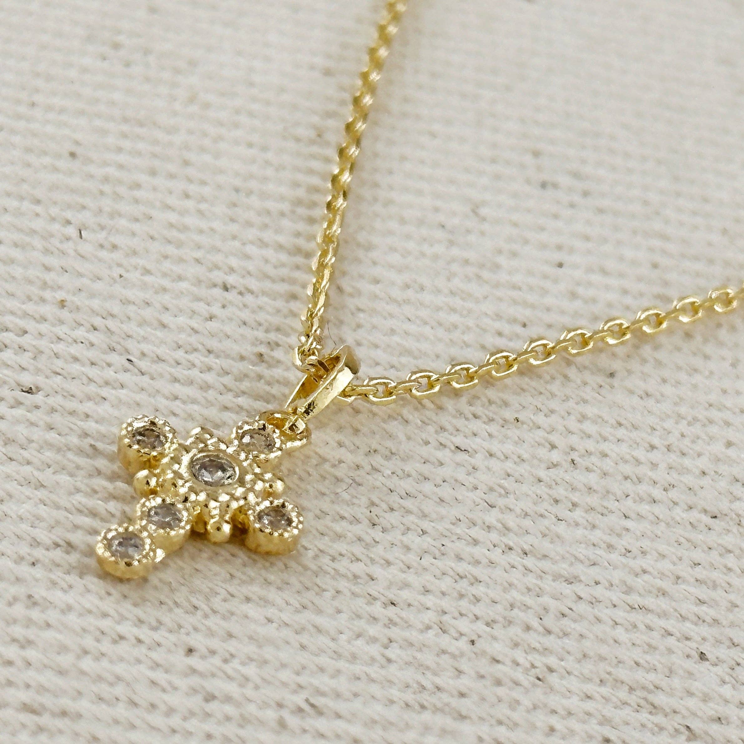 Gold necklace with a cross pendant on a textured beige background. Cross Necklace with Bezel Set CZs in 18k Gold Filled