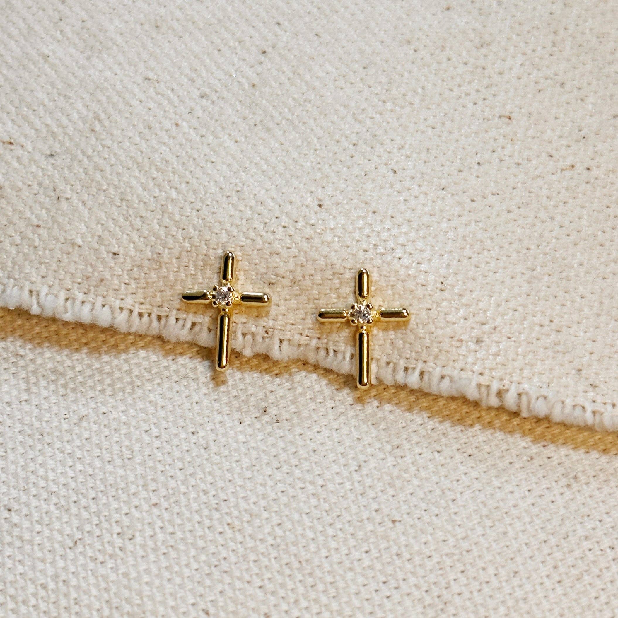 Gold cross-shaped earrings with small diamonds on a beige fabric background
