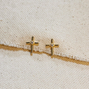 Gold cross-shaped earrings with small diamonds on a beige fabric background