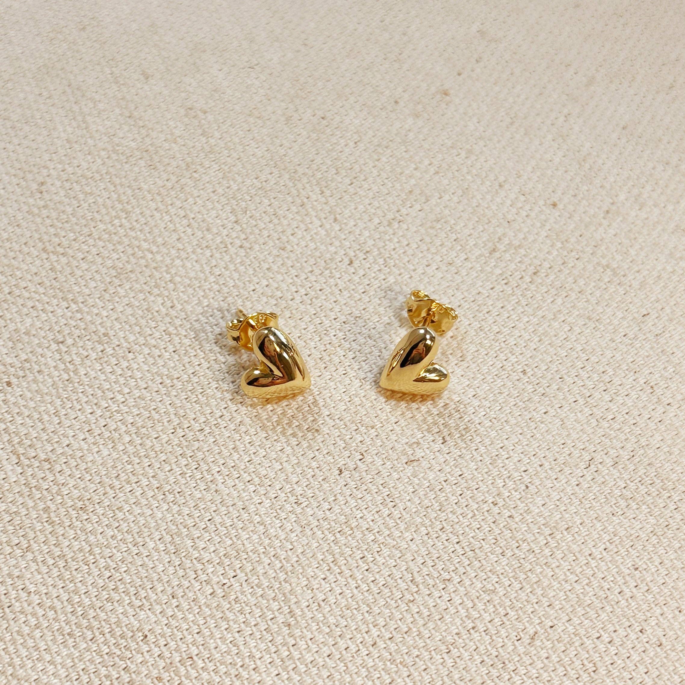 Gold heart-shaped earrings on a beige fabric background. Shop Rutledge Exchange for curated vintage and jewelry in Camden, SC.