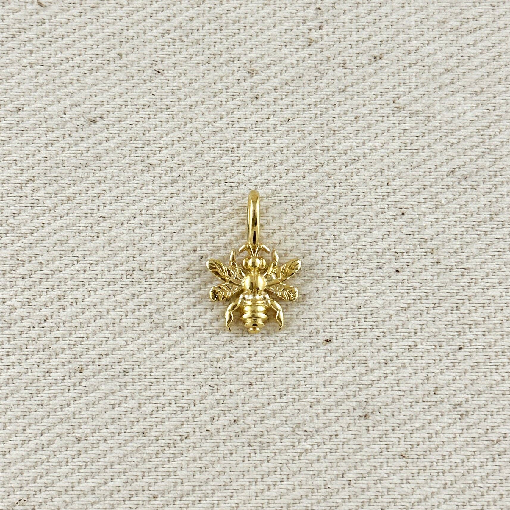 Gold bee pendant on a textured beige background. Shop Rutledge Exchange for curated vintage and jewelry in Camden, SC.&nbsp;