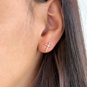 Gold cross earring worn by a person with brown hair.