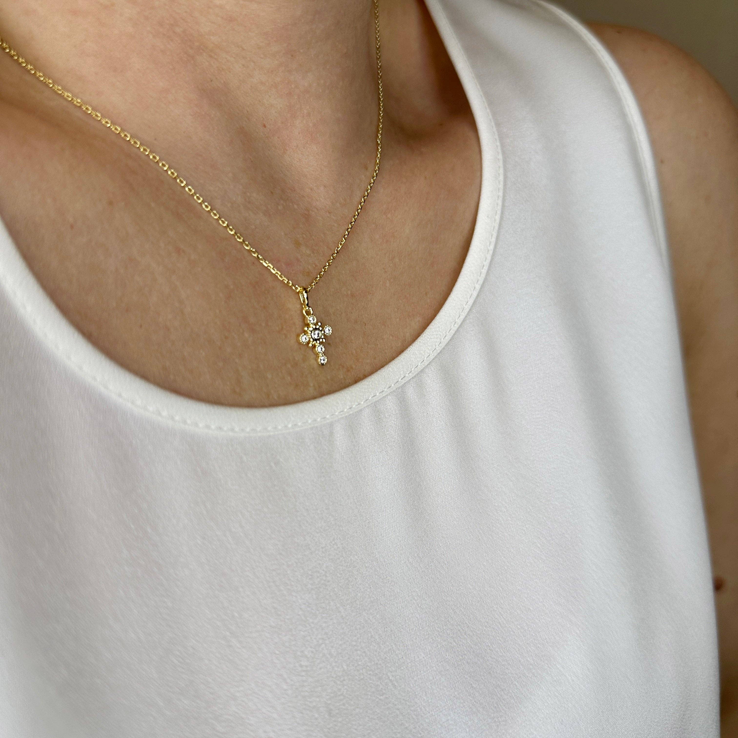 Gold necklace with a small pendant worn by a person in a white tank top. Cross Necklace with Bezel Set CZs in 18k Gold Filled