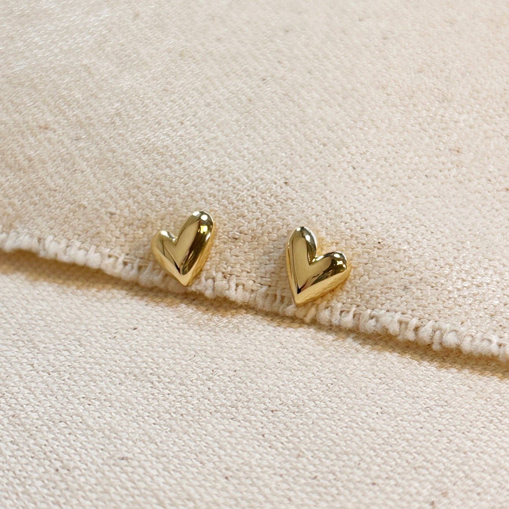 Gold heart-shaped earrings on a beige fabric background Shop Rutledge Exchange for curated vintage and jewelry in Camden, SC.