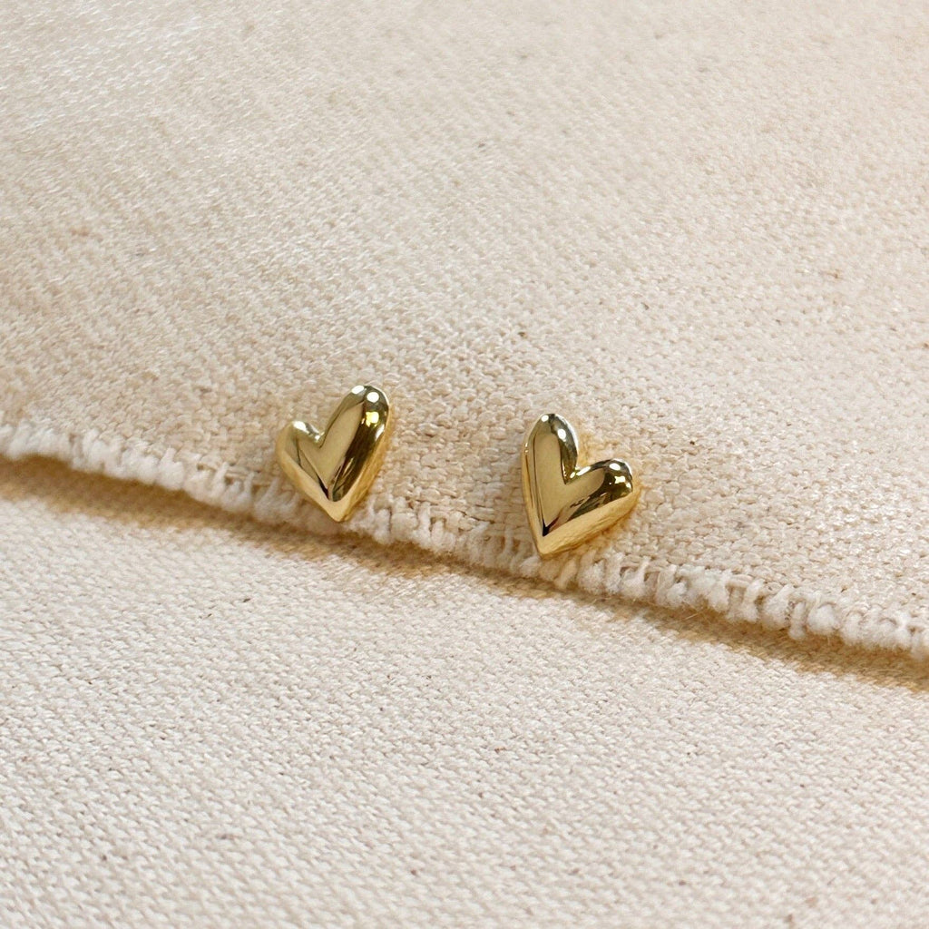 Gold heart-shaped earrings on a beige fabric background Shop Rutledge Exchange for curated vintage and jewelry in Camden, SC.