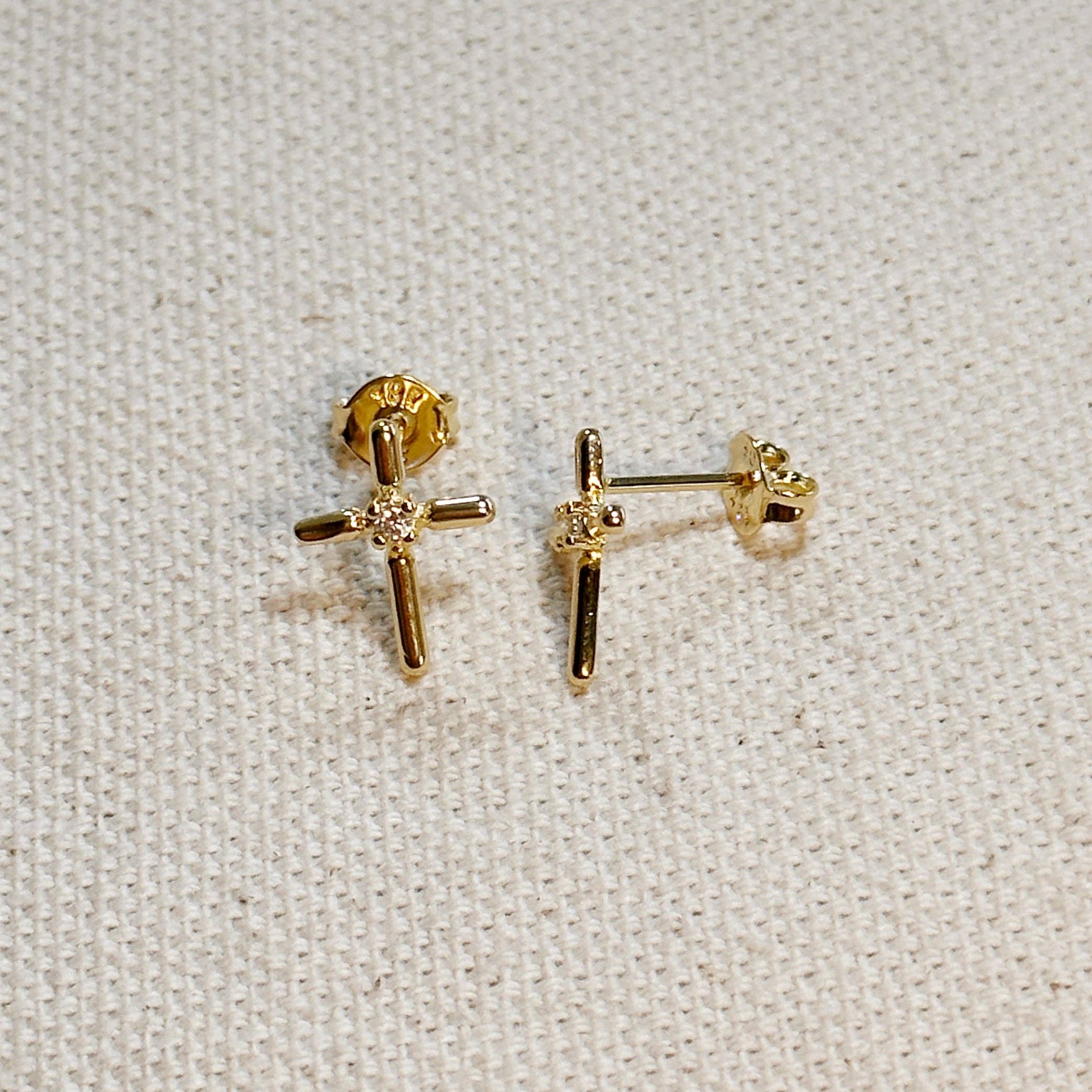 Gold cross-shaped earrings on a light fabric background