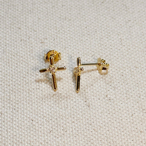 Gold cross-shaped earrings on a light fabric background