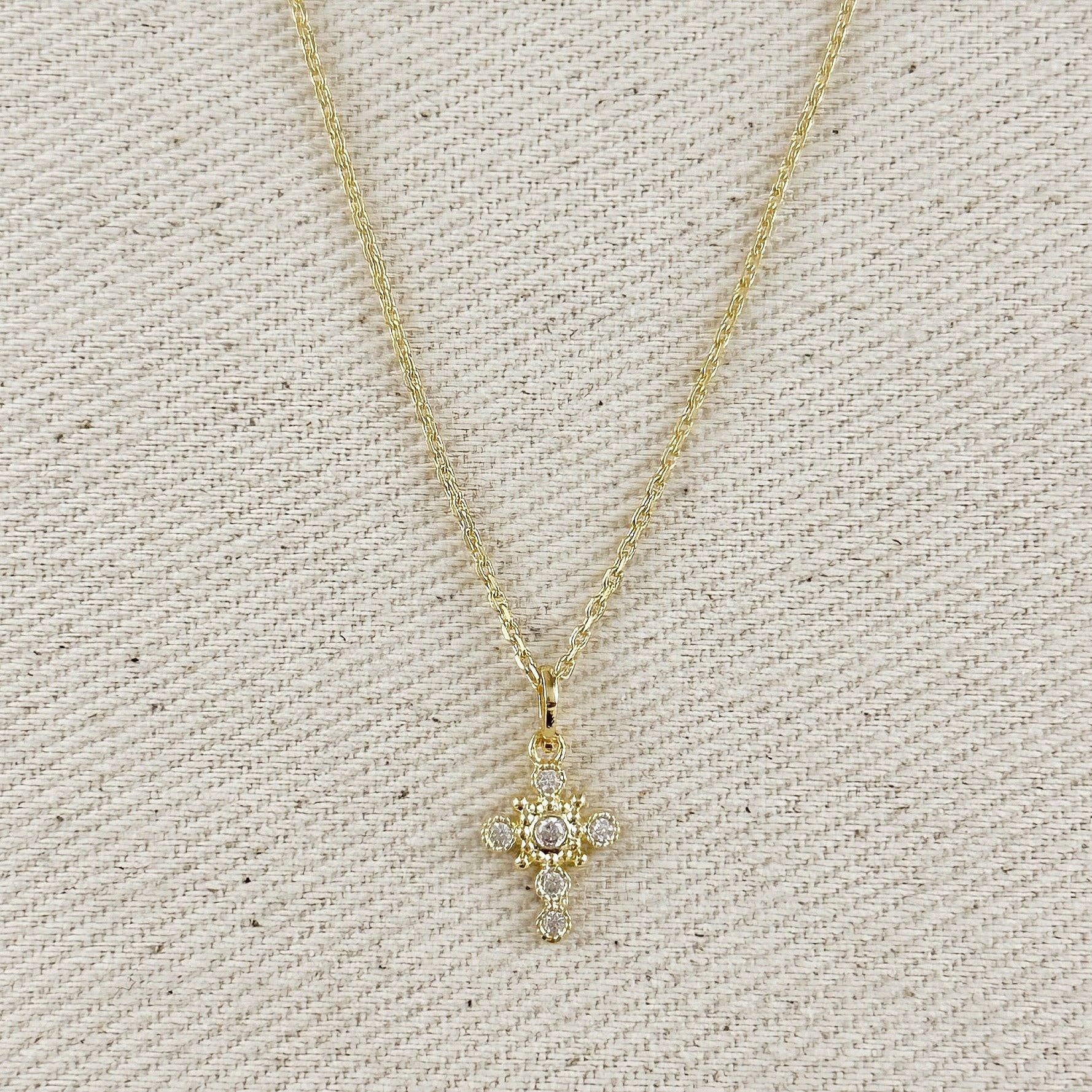 Gold necklace with a star-shaped pendant on a textured beige background. Cross Necklace with Bezel Set CZs in 18k Gold Filled