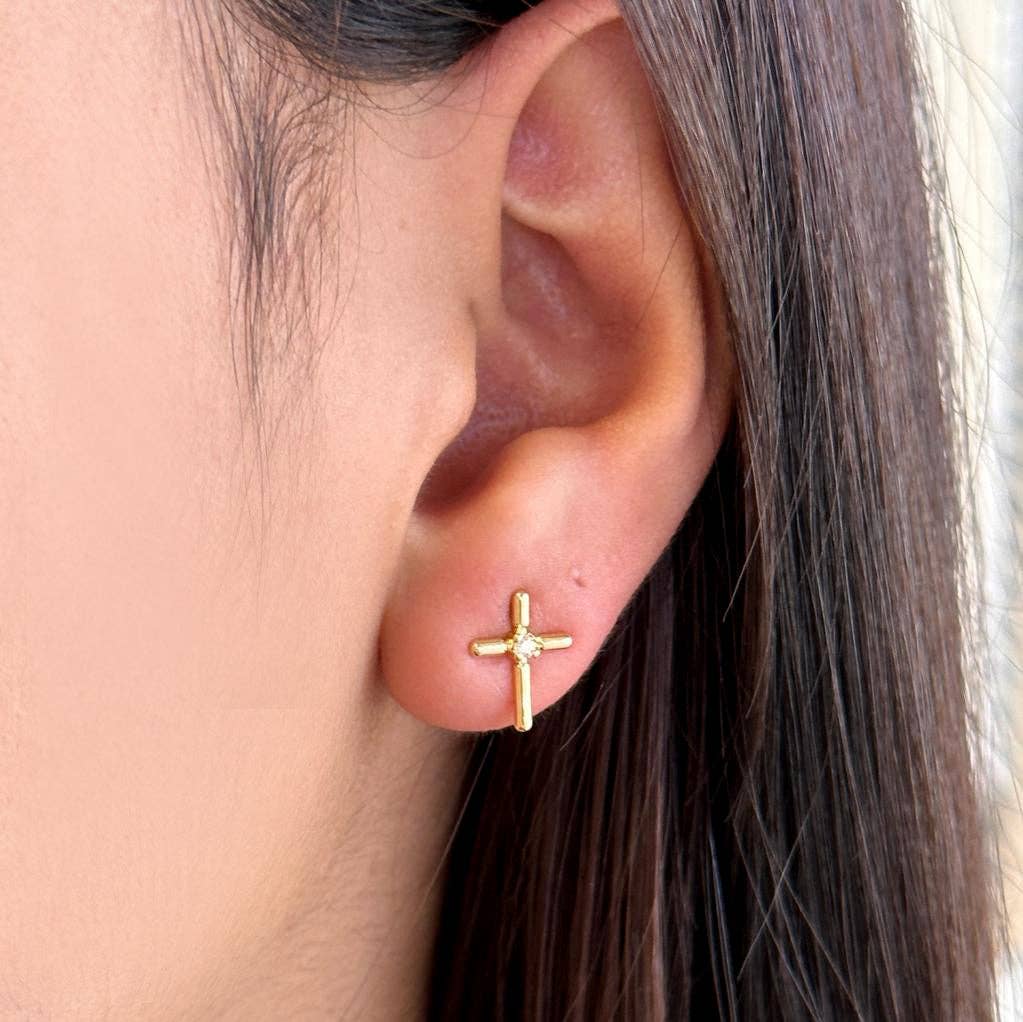 Gold cross earring worn by a person with brown hair.