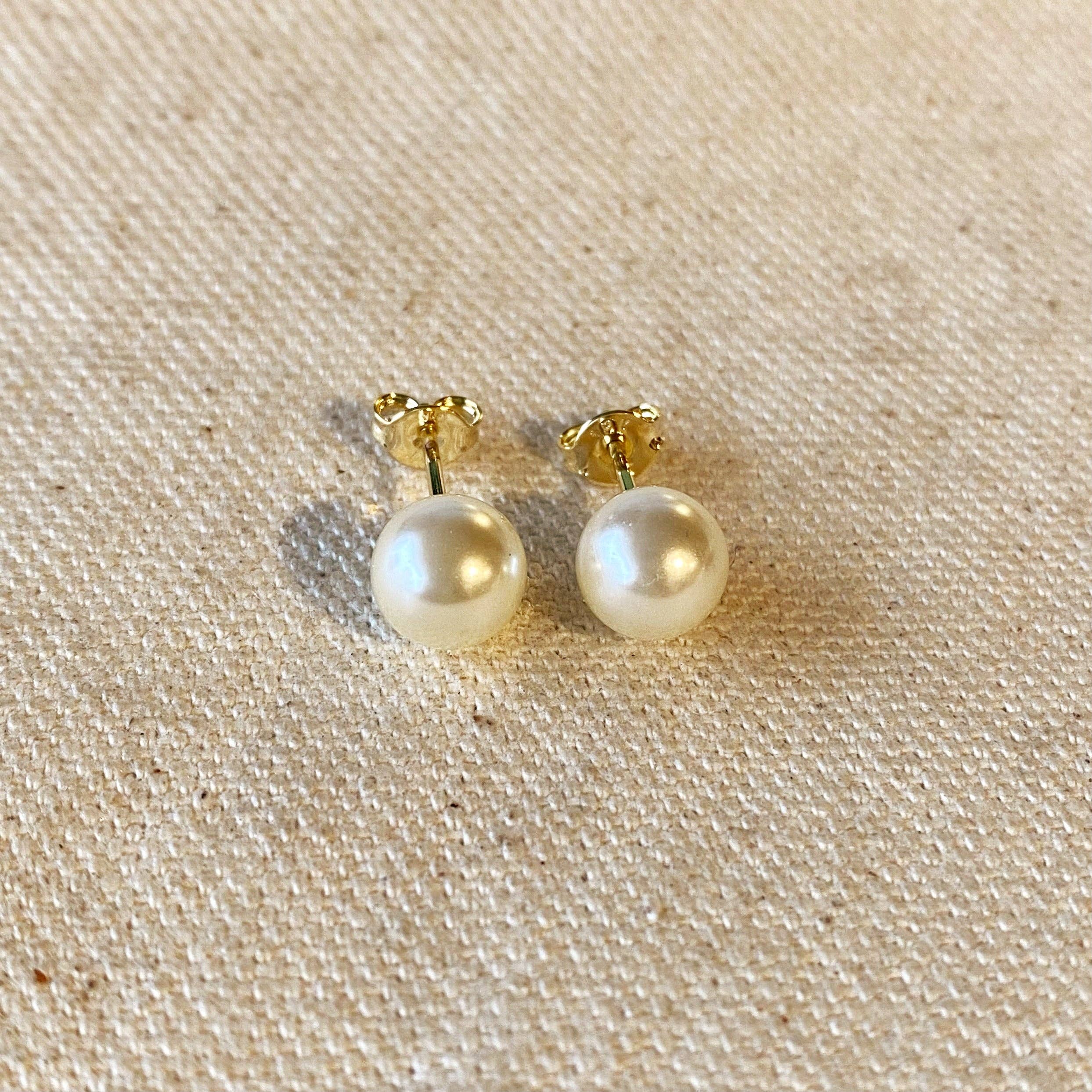 Pair of pearl earrings with gold posts on a beige fabric background. Shop Rutledge Exchange for curated vintage and jewelry in Camden, SC.