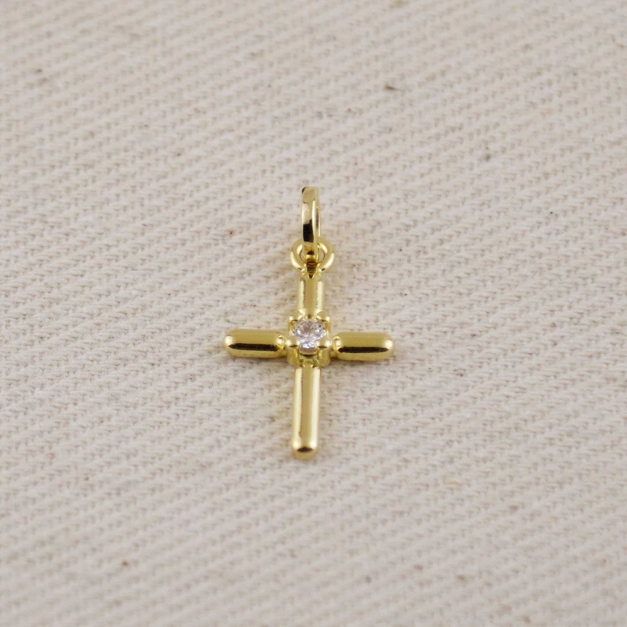 Gold cross pendant with a diamond on a beige fabric background. Shop Rutledge Exchange for curated vintage and jewelry in Camden, SC.