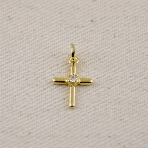 Gold cross pendant with a diamond on a beige fabric background. Shop Rutledge Exchange for curated vintage and jewelry in Camden, SC.