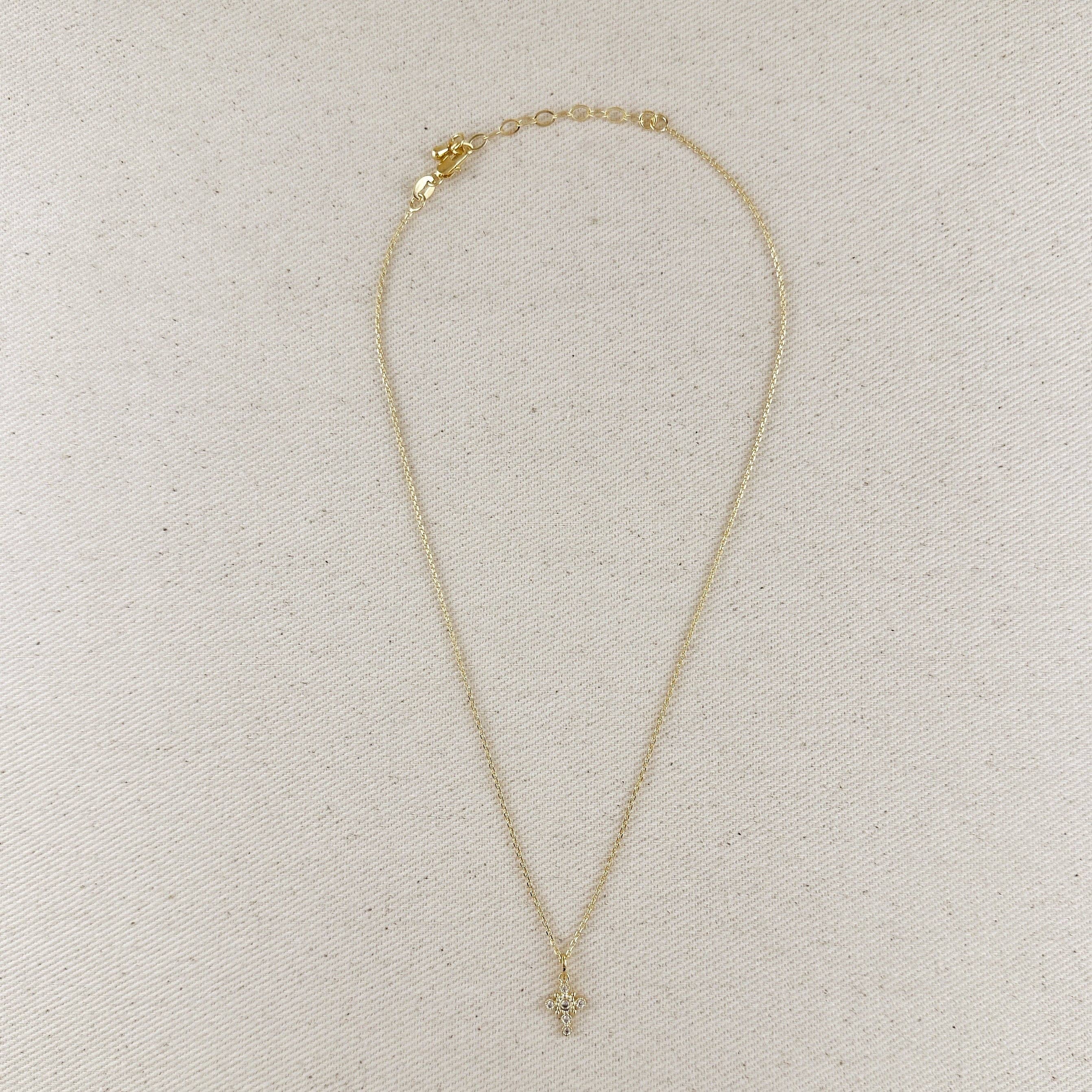 Gold necklace on a beige fabric background. Cross Necklace with Bezel Set CZs in 18k Gold Filled