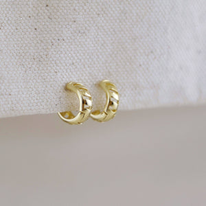 Gold hoop earrings on a textured beige surface. Shop Rutledge Exchange for curated vintage and jewelry in Camden, SC.
