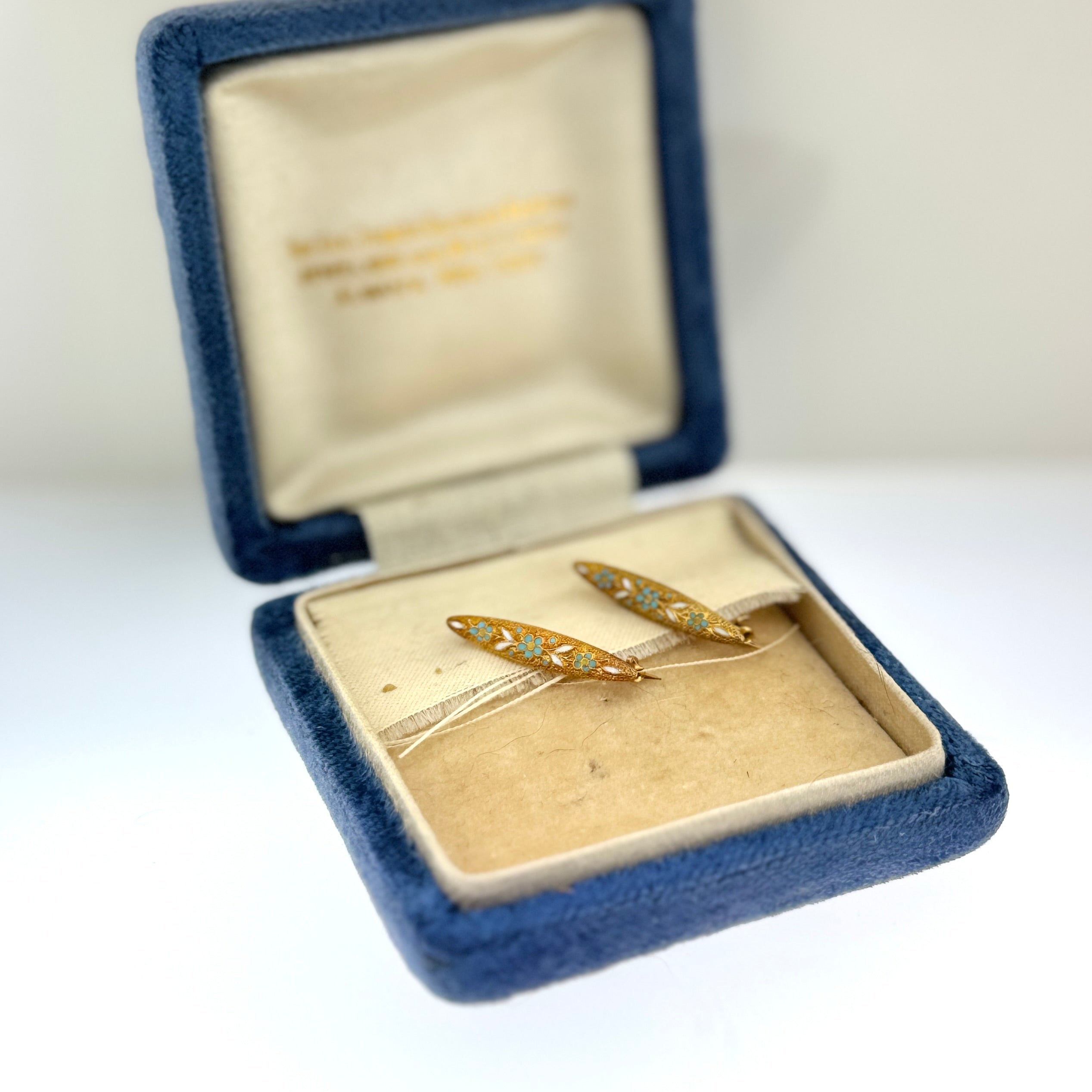 Gold brooches in an open blue velvet jewelry box on a white background at Rutledge Exchange in Camden SC