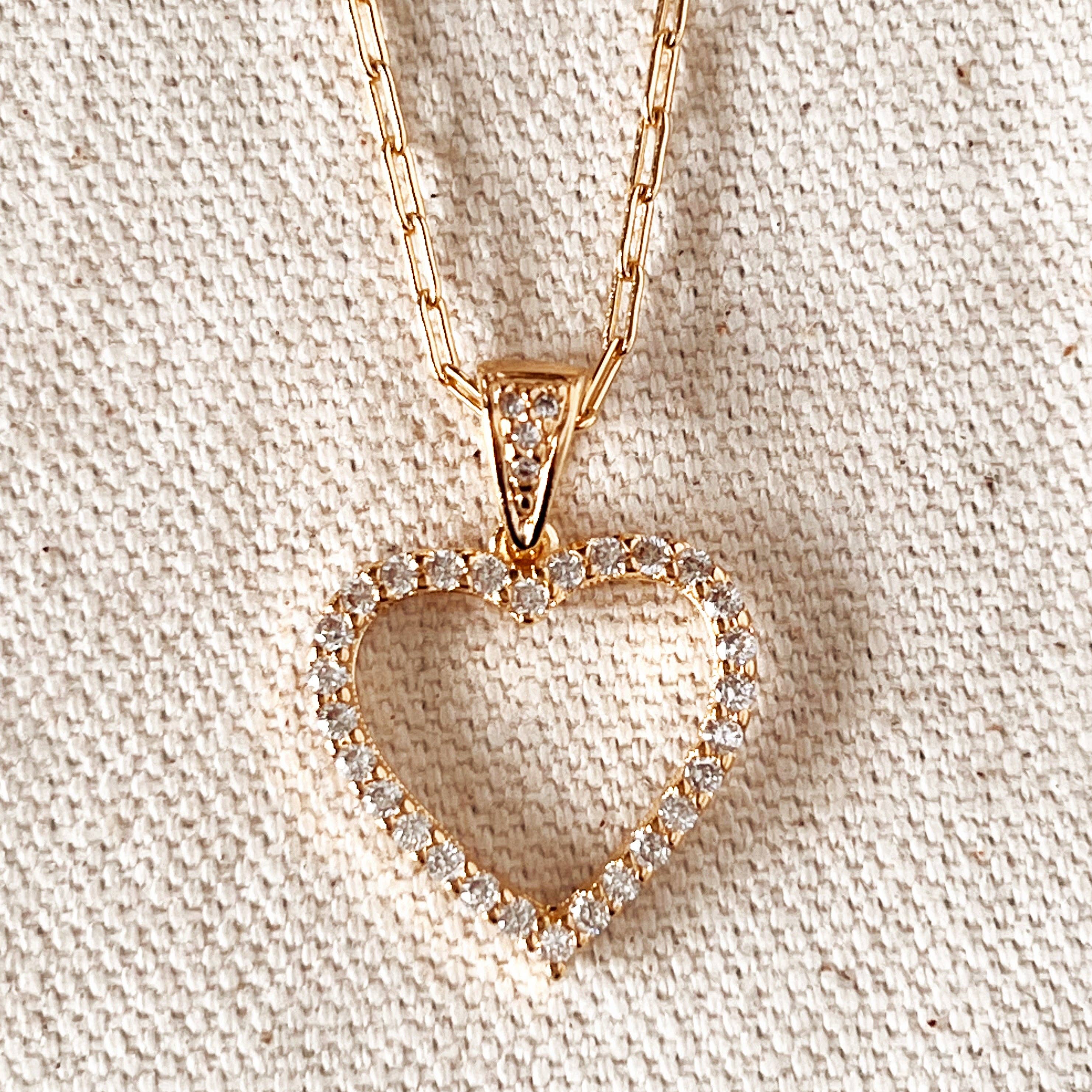 Heart-shaped diamond pendant on a gold chain against a beige fabric background. Shop Rutledge Exchange for curated vintage and jewelry in Camden, SC.