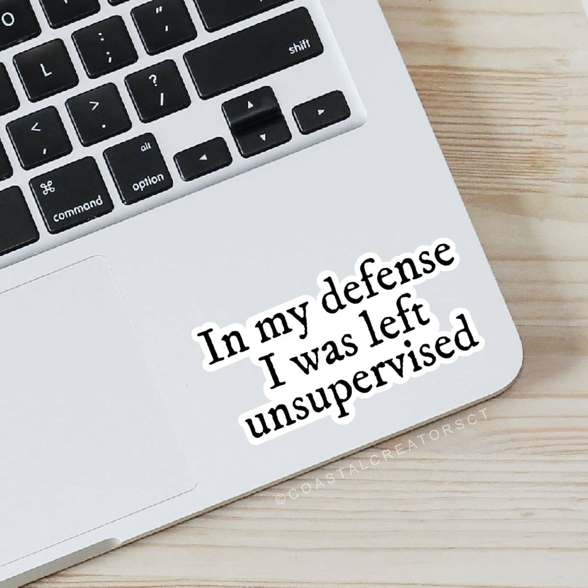Laptop with a sticker reading 'In my defense I was left unsupervised' on a wooden surface