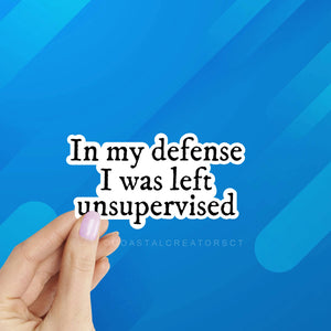 Text 'In my defense I was left unsupervised' held by a hand against a blue geometric background. In My Defense I Was Left Unsupervised Laptop Kindle Sticker