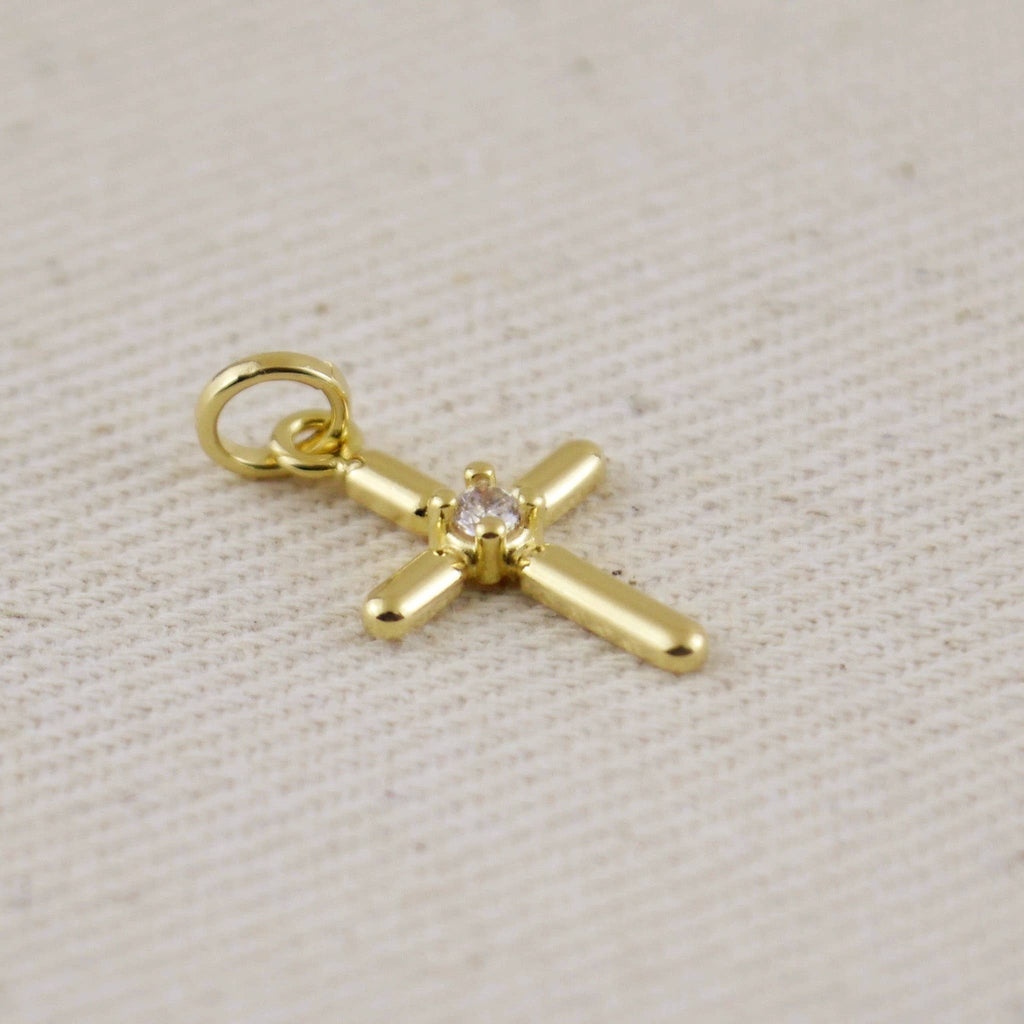 Gold cross pendant with a small diamond on a beige fabric background Shop Rutledge Exchange for curated vintage and jewelry in Camden, SC.