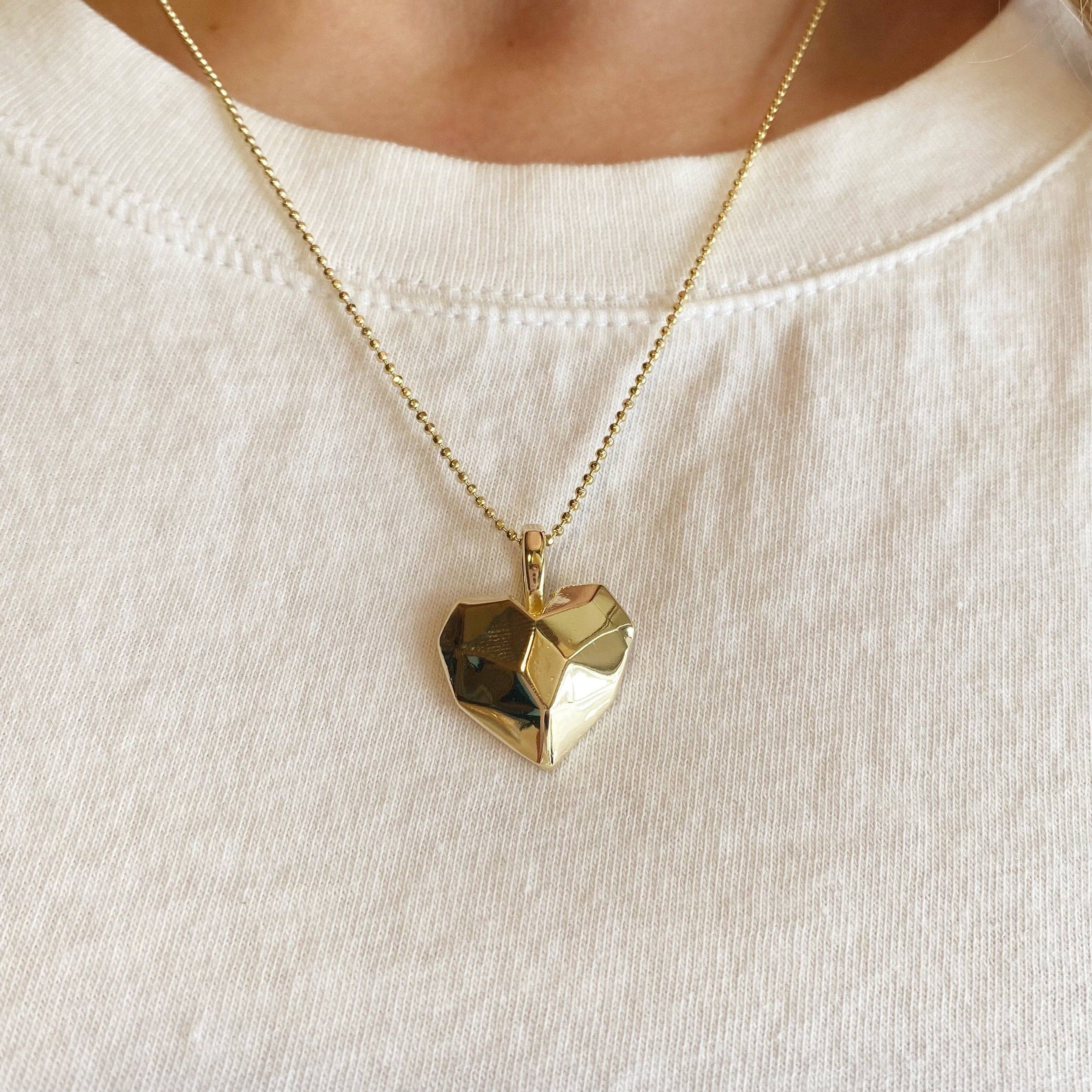 Gold heart-shaped pendant necklace on a white shirt . Shop Rutledge Exchange for curated vintage and jewelry in Camden, SC.