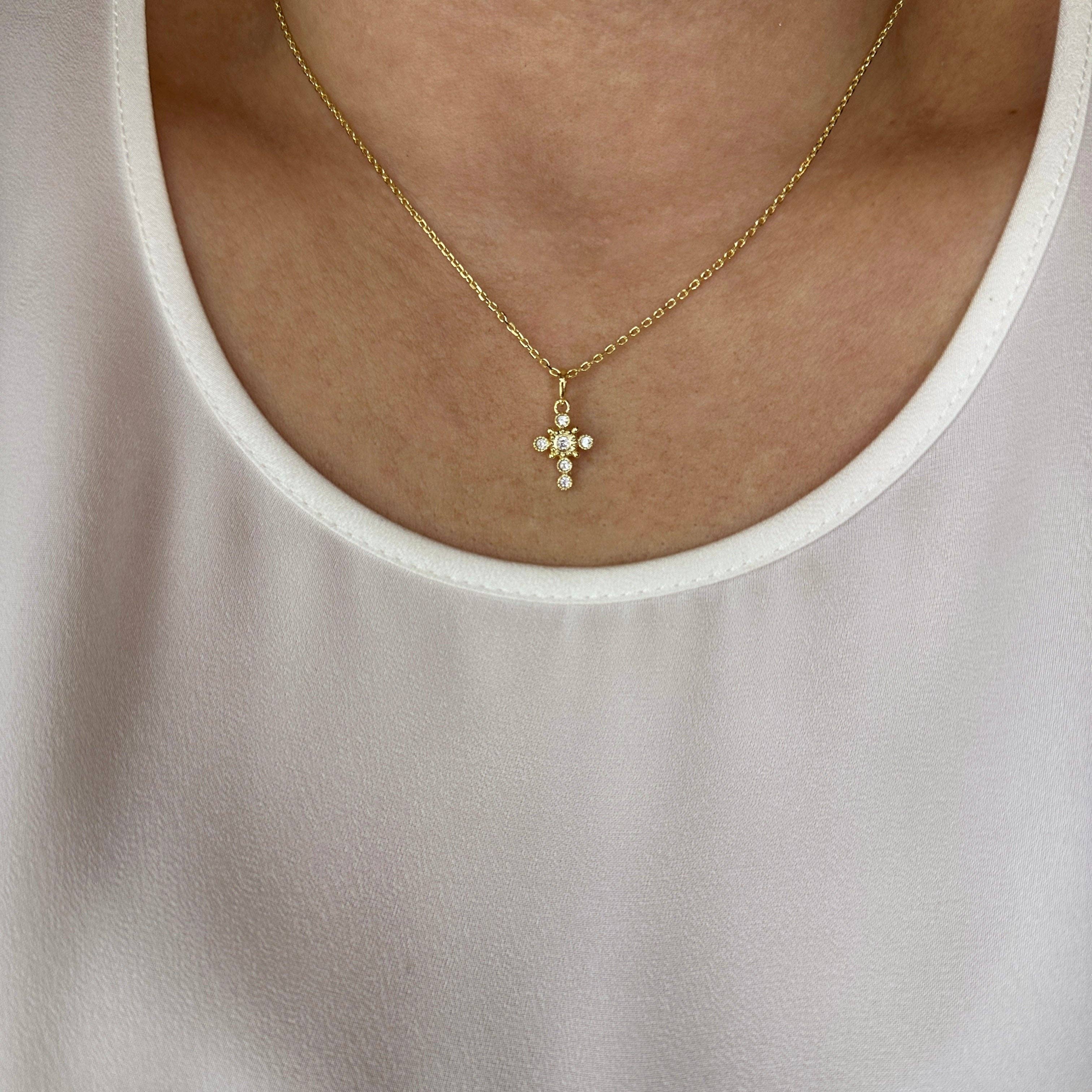 Gold necklace with a cross pendant worn by a person in a light-colored top. Cross Necklace with Bezel Set CZs in 18k Gold Filled
