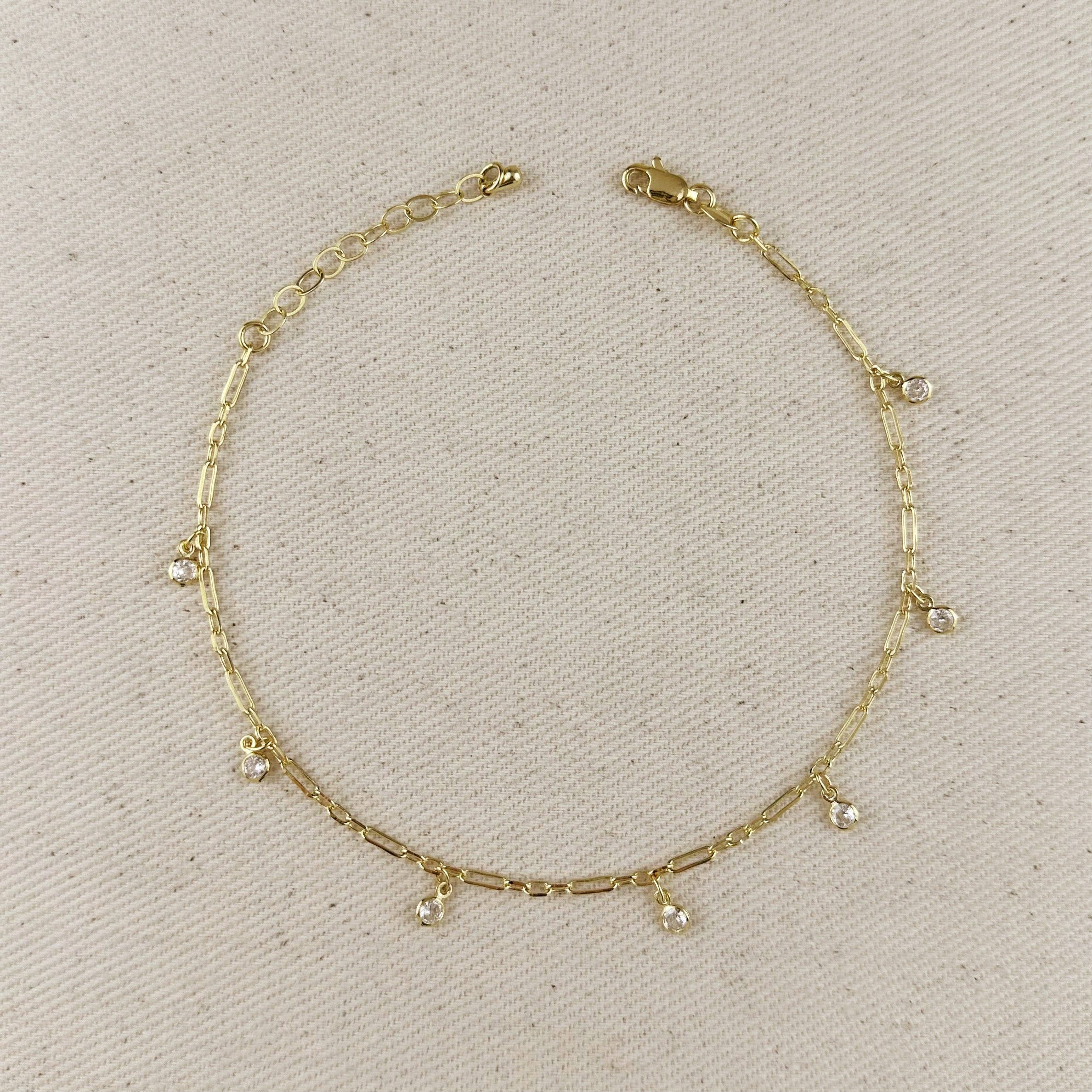 Gold anklet with small dangling charms on a beige fabric background at Shop Rutledge Exchange for curated vintage and jewelry in Camden, SC.&nbsp;